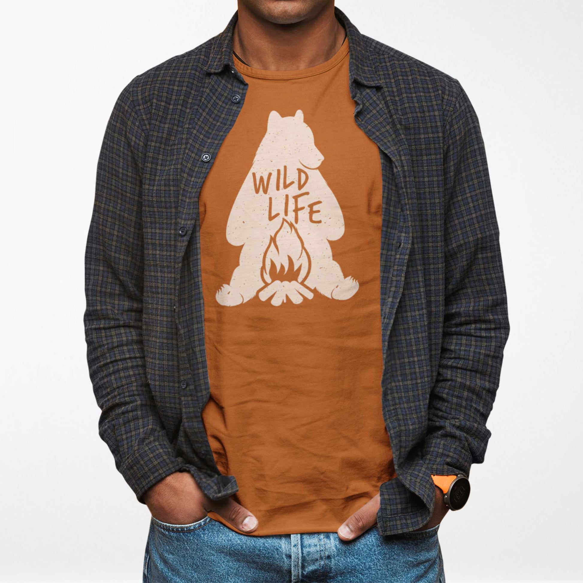 A man wearing an autumn burnt orange Bella Canvas t-shirt featuring a silhouette of a grizzly bear sitting in front of a campfire with the words wild life.