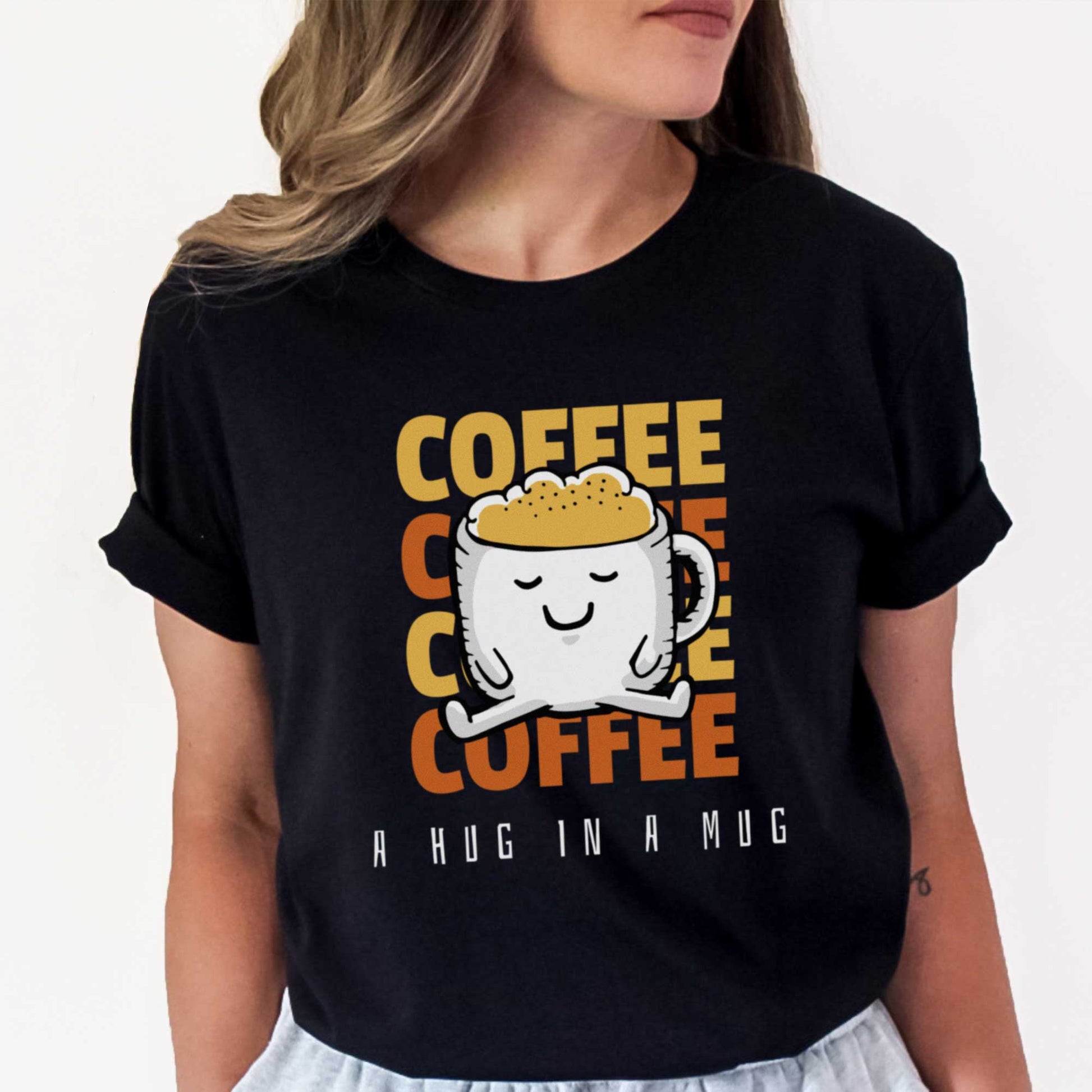A woman wearing a black Bella Canvas t-shirt featuring a cartoon mug full of coffee and the words coffee a hug in a mug.
