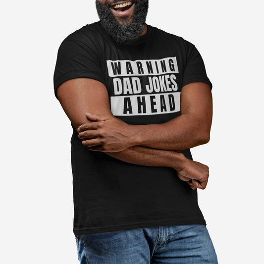 A man wearing a black Bella Canvas t-shirt featuring the words warning dad jokes ahead.
