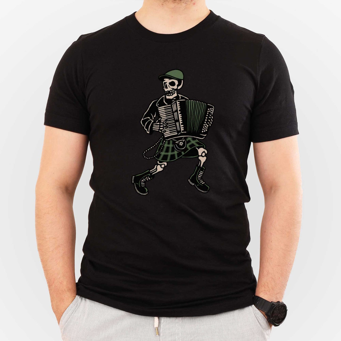 A man wearing a black Bella Canvas t-shirt featuring a skeleton dressed in Irish garb and playing an accordion.