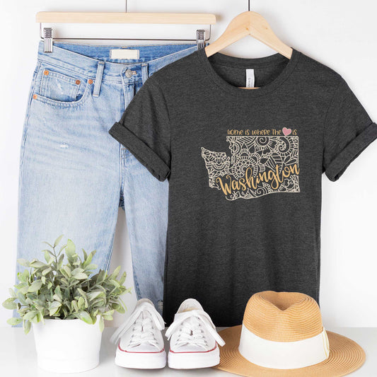 A hanging dark grey heather Bella Canvas t-shirt featuring a mandala in the shape of Washington with the words home is where the heart is.