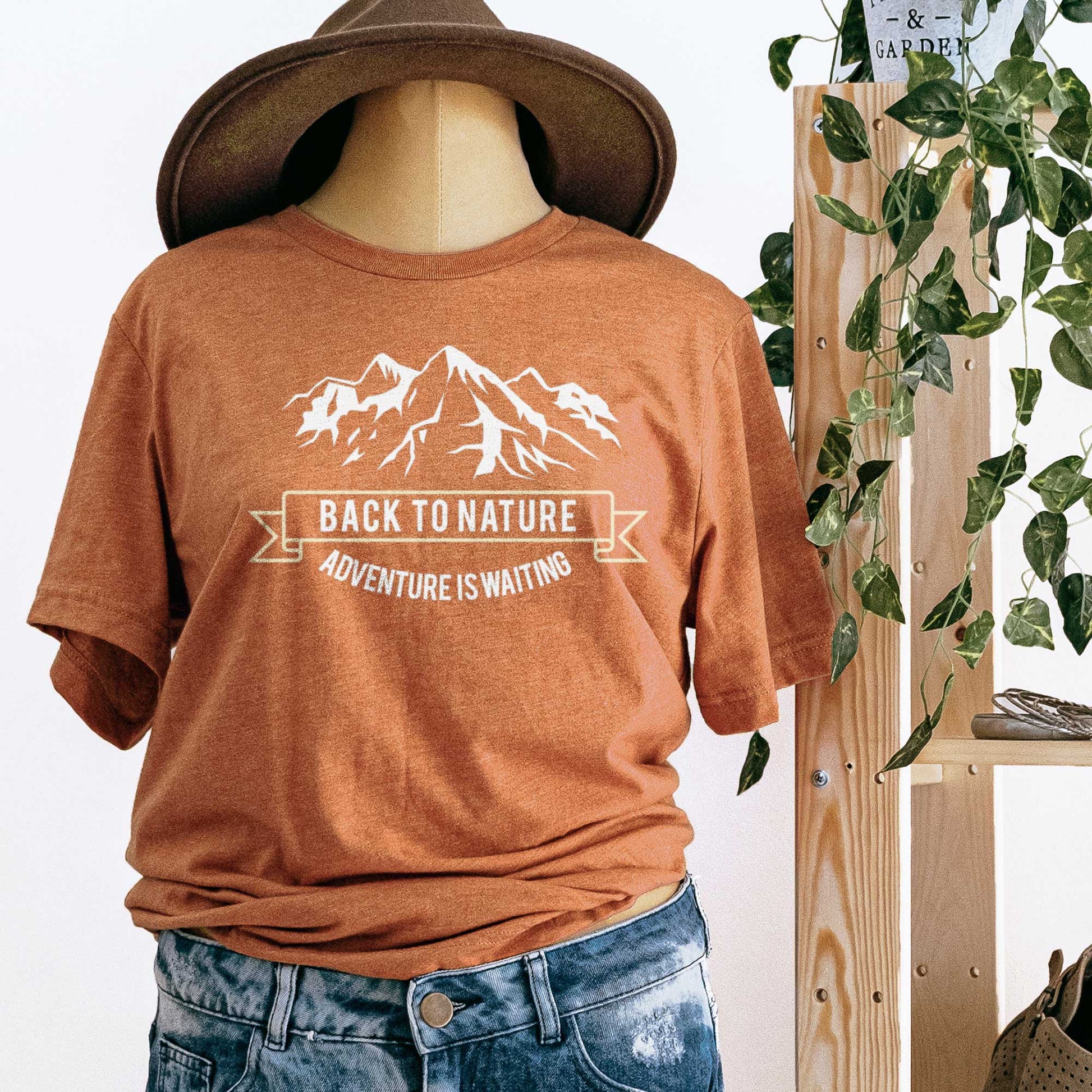A mannequin wearing heather autumn Bella Canvas t-shirt that says back to nature with mountains.