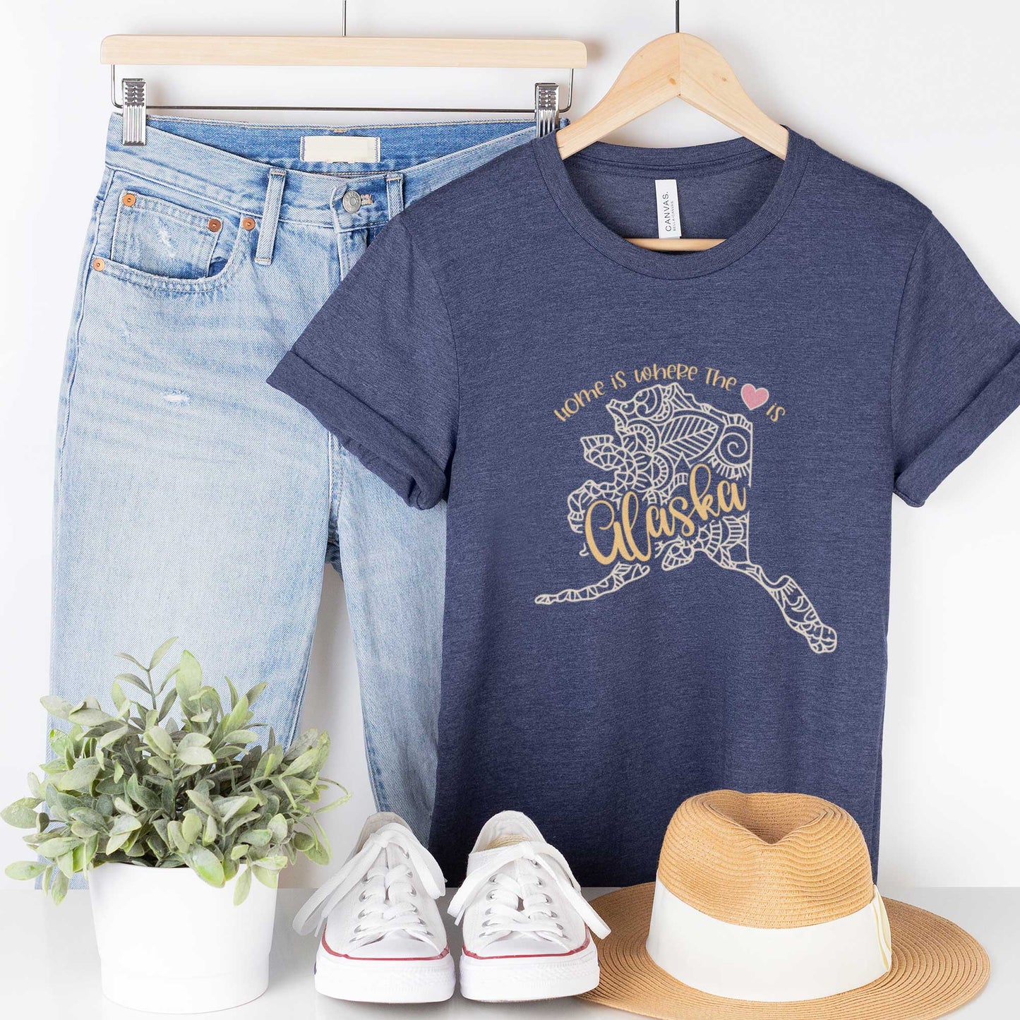 A hanging heather navy Bella Canvas t-shirt featuring a mandala in the shape of Alaska with the words home is where the heart is.