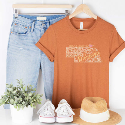 A hanging heather autumn Bella Canvas t-shirt featuring a mandala in the shape of Nebraska with the words home is where the heart is.