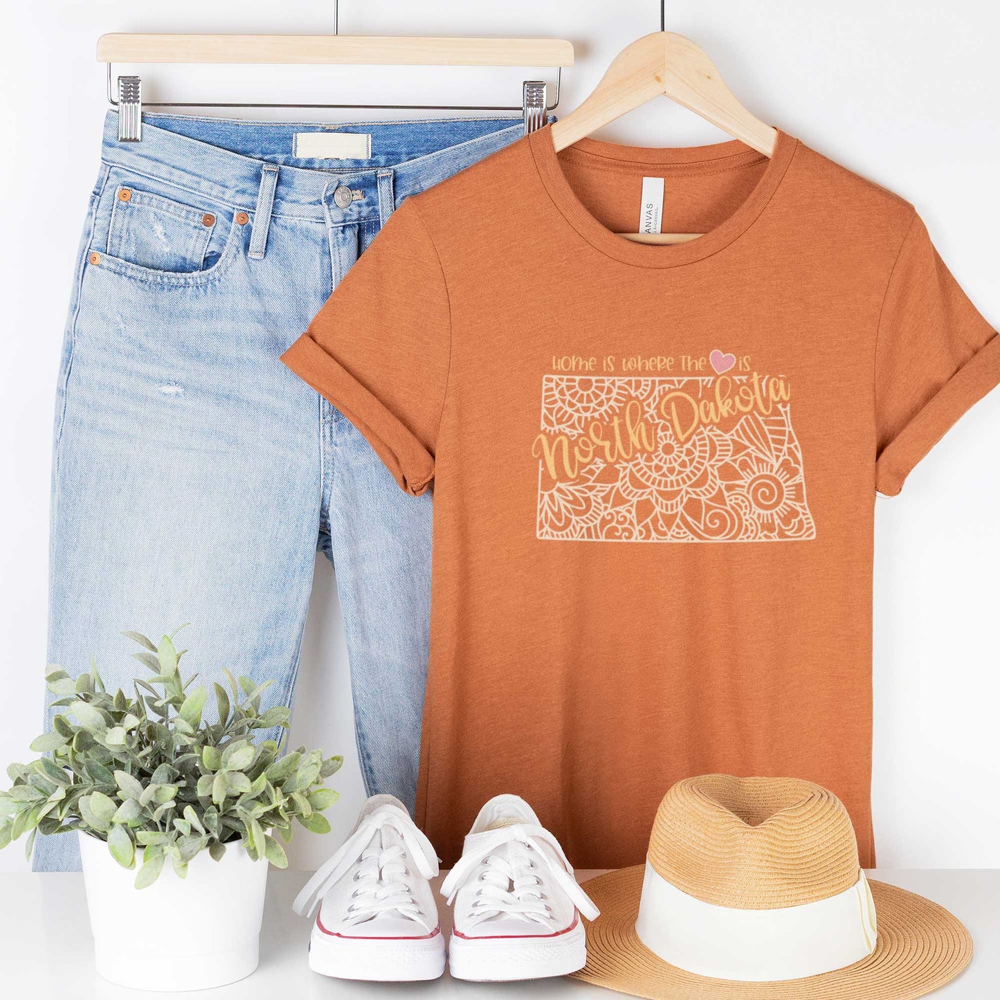 A hanging heather autumn Bella Canvas t-shirt featuring a mandala in the shape of North Dakota with the words home is where the heart is.