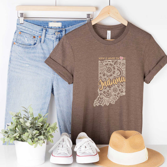 A hanging heather brown Bella Canvas t-shirt featuring a mandala in the shape of Indiana with the words home is where the heart is.