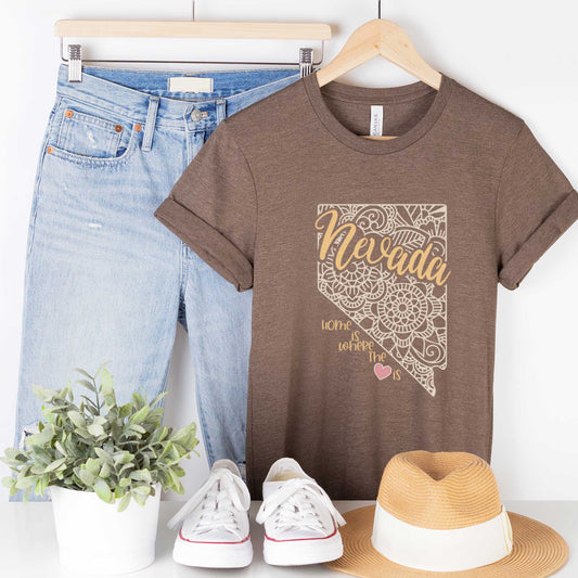 A hanging heather brown Bella Canvas t-shirt featuring a mandala in the shape of Nevada with the words home is where the heart is.