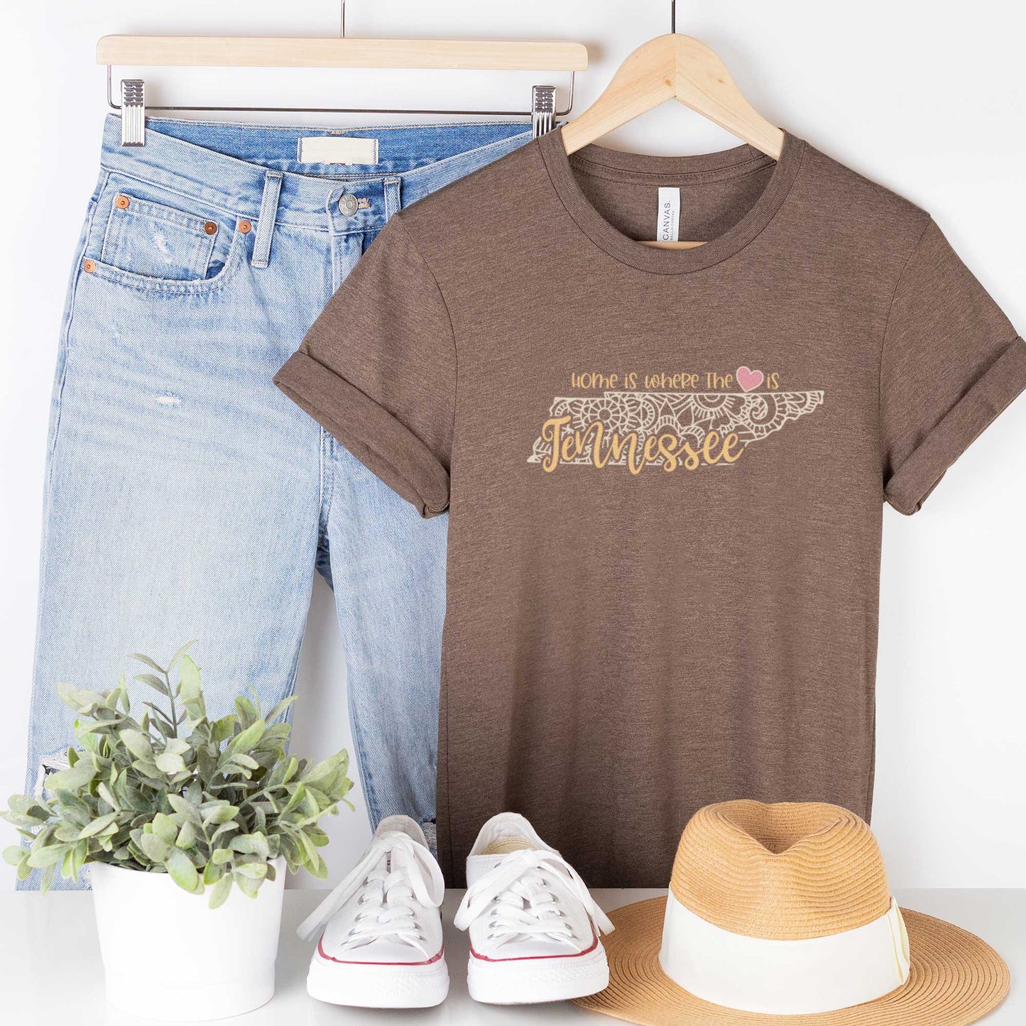A hanging heather brown Bella Canvas t-shirt featuring a mandala in the shape of Tennessee with the words home is where the heart is.
