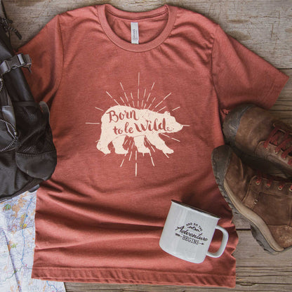 A heather clay Bella Canvas t-shirt surrounded by hiking gear with a bear and the words born to be wild.