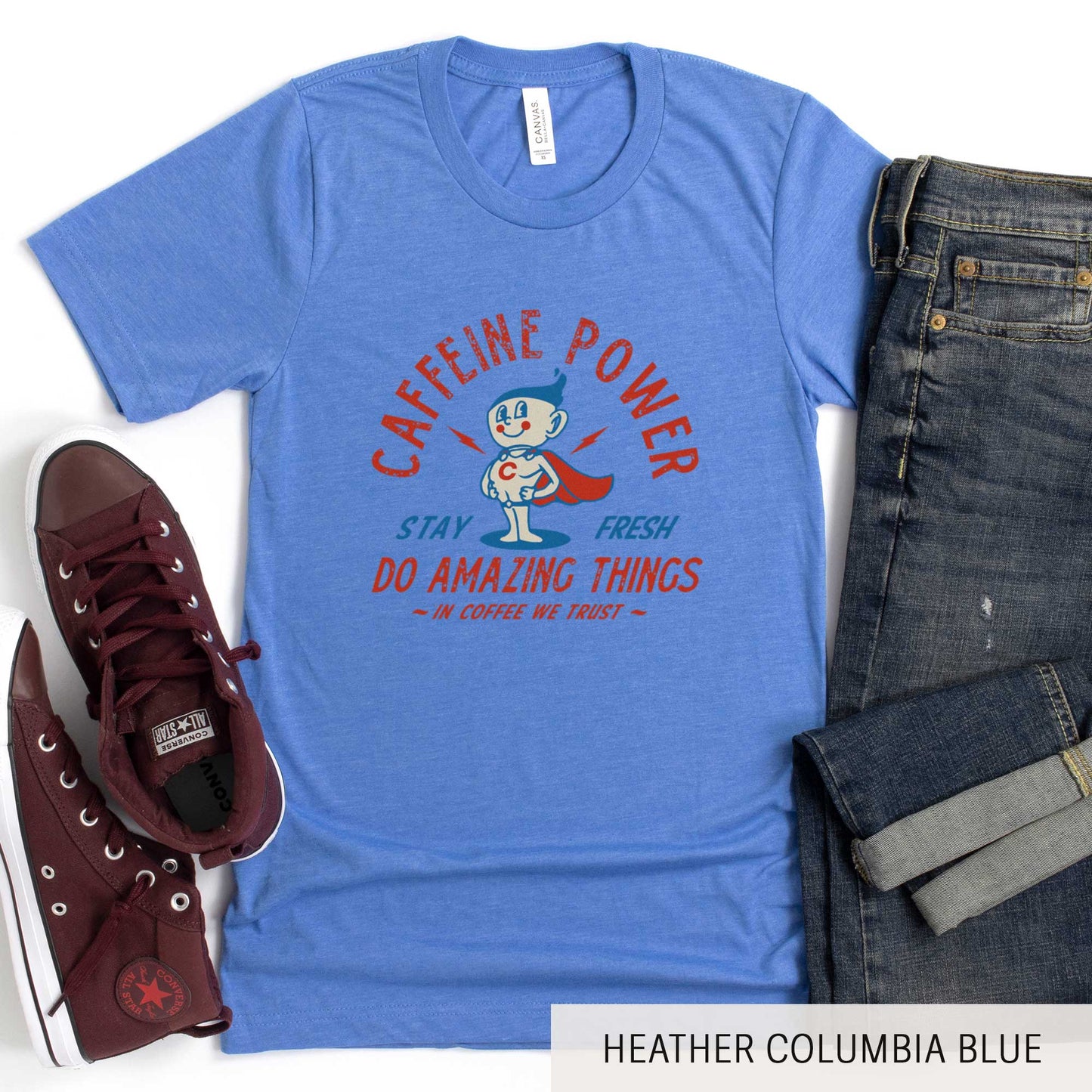 A heather columbia blue Bella Canvas t-shirt featuring a retro coffee mug dressed as a super hero with the words caffeine power, stay fresh, do amazing things, in coffee we trust.