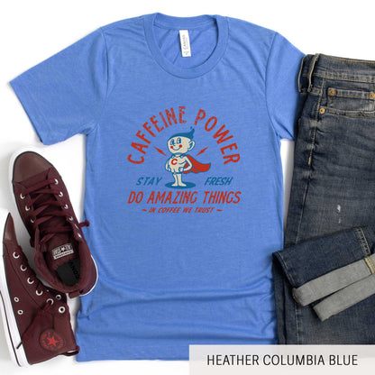 A heather columbia blue Bella Canvas t-shirt featuring a retro coffee mug dressed as a super hero with the words caffeine power, stay fresh, do amazing things, in coffee we trust.