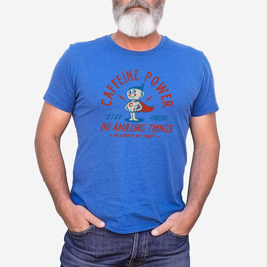 A man wearing a heather columbia blue Bella Canvas t-shirt featuring a retro coffee mug dressed as a super hero with the words caffeine power, stay fresh, do amazing things, in coffee we trust.