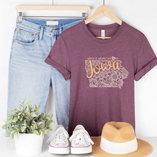 A hanging heather maroon Bella Canvas t-shirt featuring a mandala in the shape of Iowa with the words home is where the heart is.