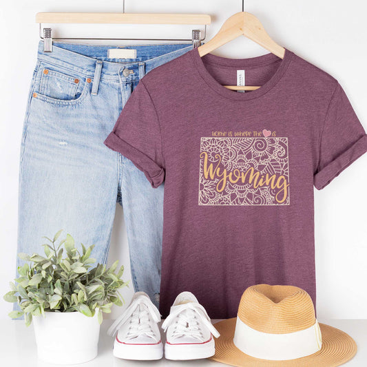 A hanging heather maroon Bella Canvas t-shirt featuring a mandala in the shape of Wyoming with the words home is where the heart is.