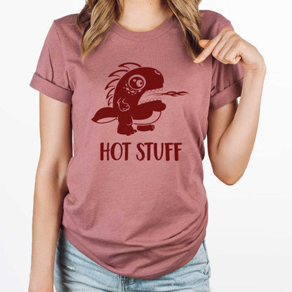 A woman wearing a heather mauve Bella Canvas t-shirt wearing a cute cartoon monster that is belching fire with the words hot stuff.