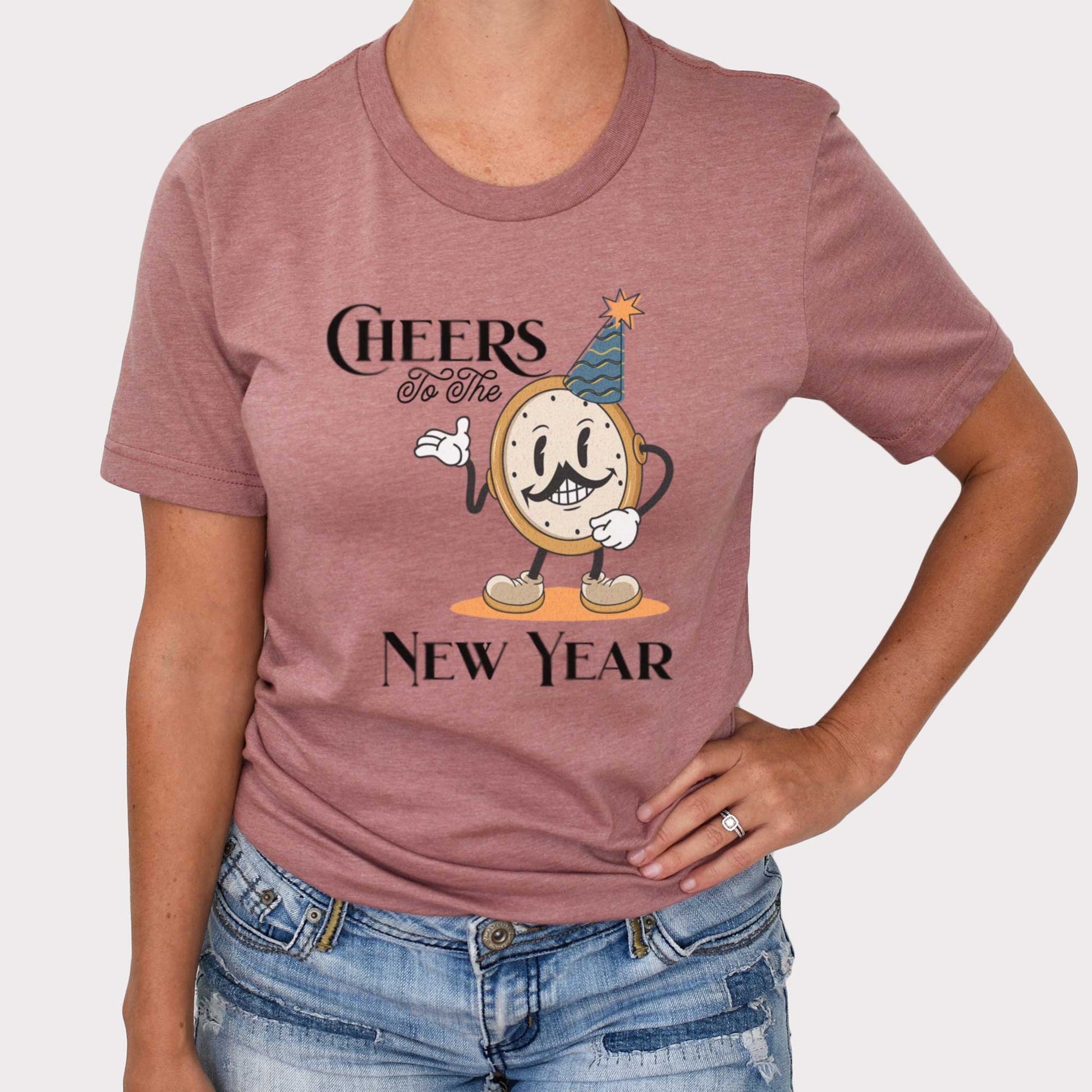 A woman wearing a heather mauve Bella Canvas t-shirt featuring a retro looking clock cartoon with a party hat next to the words Cheers to the New Year.
