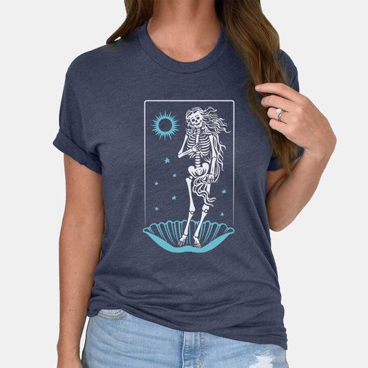 A woman wearing a heather navy Bella Canvas t-shirt that features a skeleton in a pose similar to Botticelli's Birth of Venus painting.