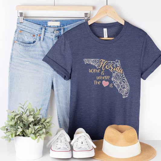 A hanging heather navy Bella Canvas t-shirt featuring a mandala in the shape of Florida with the words home is where the heart is.