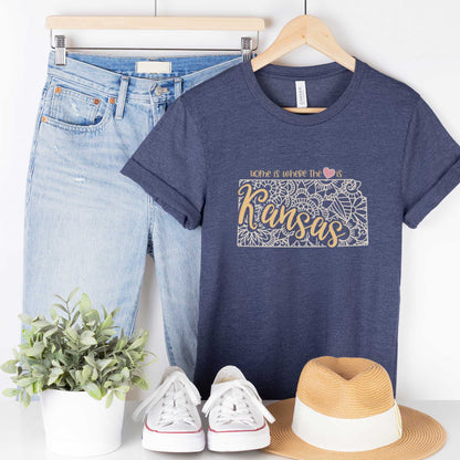 A hanging heather navy Bella Canvas t-shirt featuring a mandala in the shape of Kansas with the words home is where the heart is.