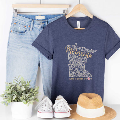 A hanging heather navy Bella Canvas t-shirt featuring a mandala in the shape of Minnesota with the words home is where the heart is.