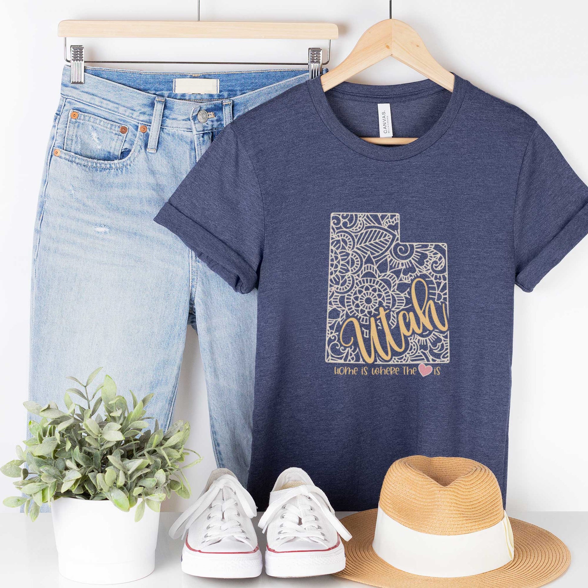 A hanging heather navy Bella Canvas t-shirt featuring a mandala in the shape of Utah with the words home is where the heart is.