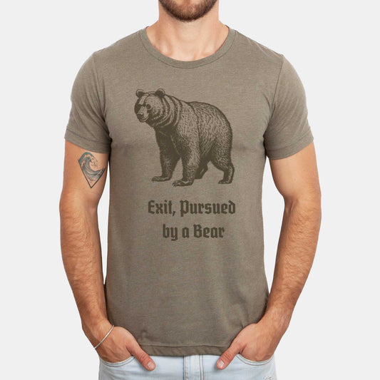 A man wearing a heather olive Bella Canvas t-shirt featuring a vintage looking bear with the words exit, pursued by a bear.