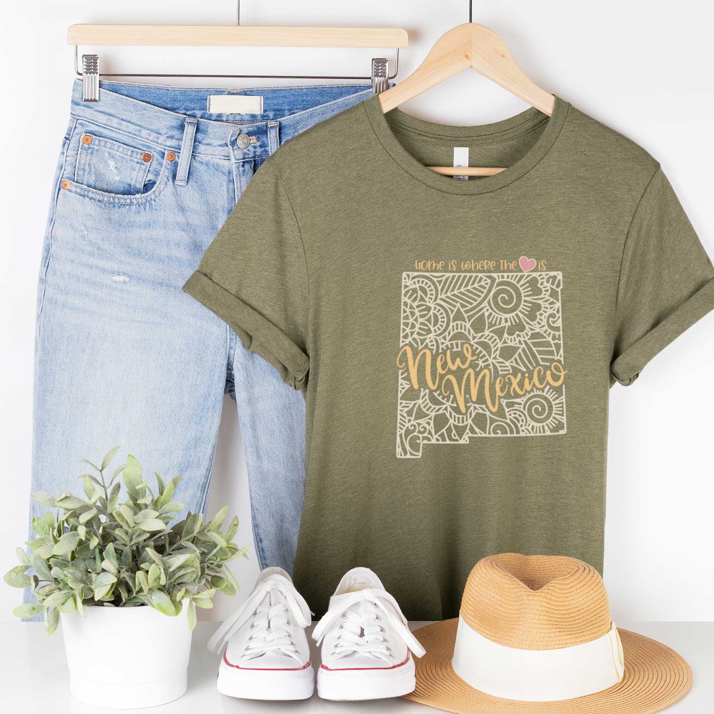 A hanging heather olive Bella Canvas t-shirt featuring a mandala in the shape of New Mexico with the words home is where the heart is.