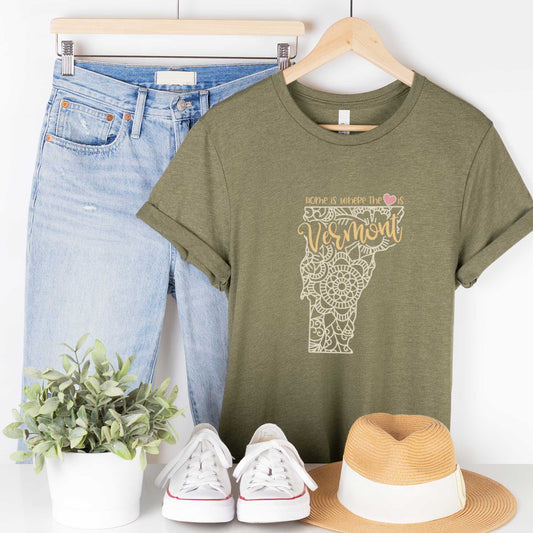 A hanging heather olive Bella Canvas t-shirt featuring a mandala in the shape of Vermont with the words home is where the heart is.