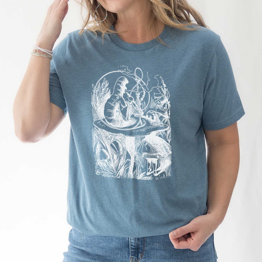 A woman wearing a heather slate Bella Canvas t-shirt featuring the John Tenniel illustration of Alice in Wonderland meeting the caterpillar who is sitting on a mushroom.