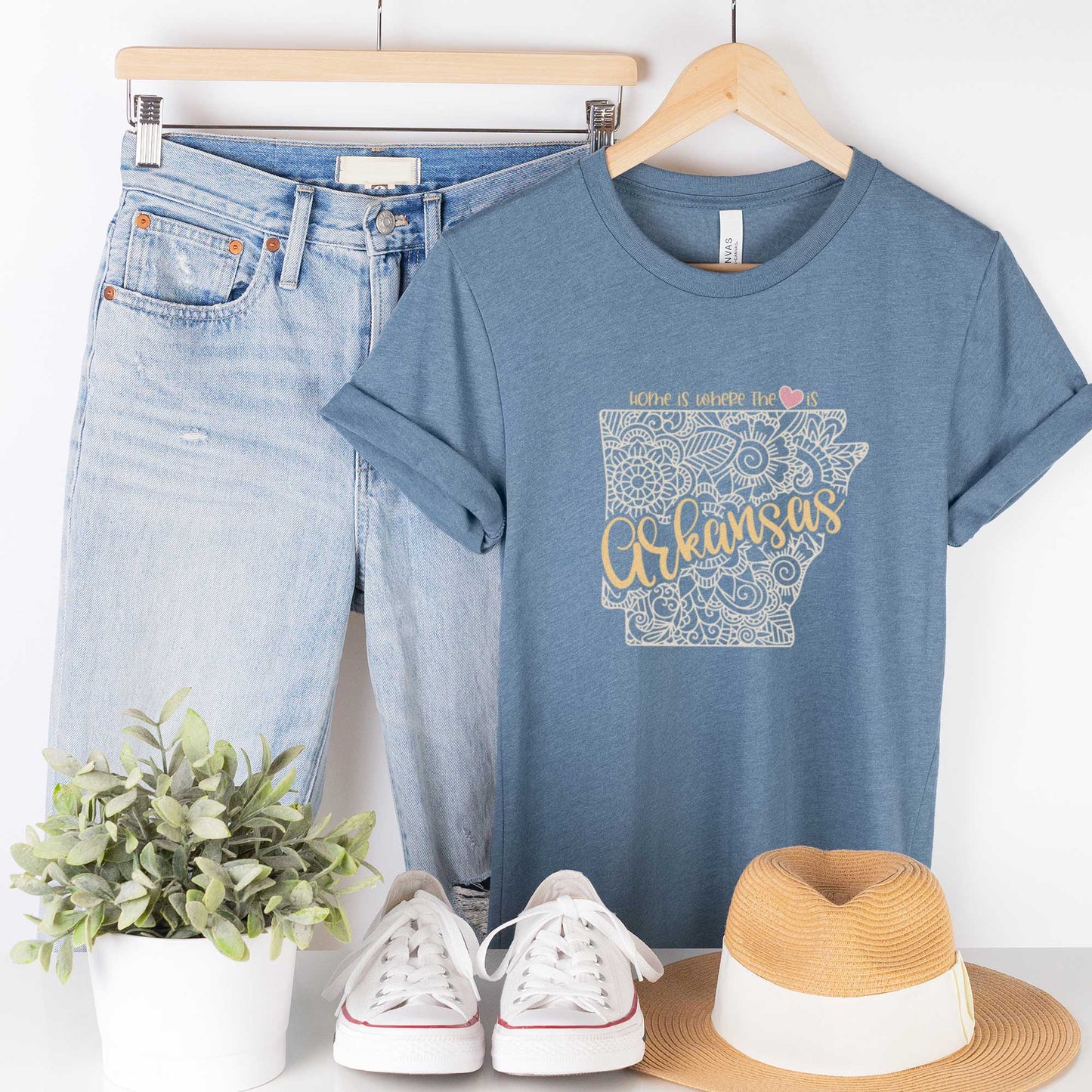 A hanging heather slate Bella Canvas t-shirt featuring a mandala in the shape of Arkansas with the words home is where the heart is.