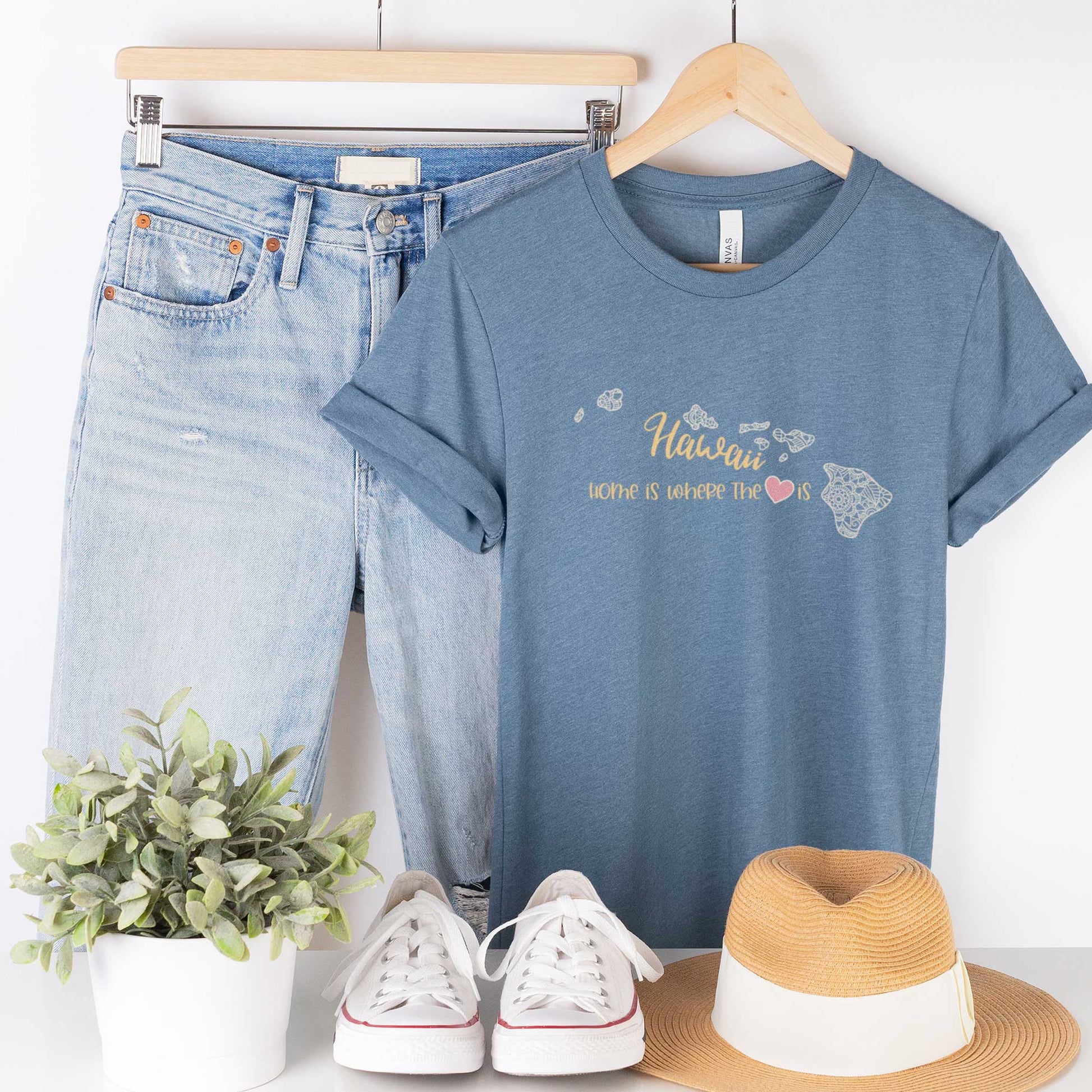 A hanging heather slate Bella Canvas t-shirt featuring a mandala in the shape of Hawaii with the words home is where the heart is.