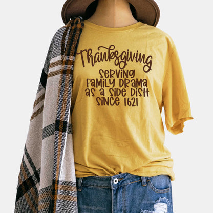 A mannequin wearing a mustard yellow Bella Canvas t-shirt featuring the words thanksgiving serving family as a side dish since 1621.