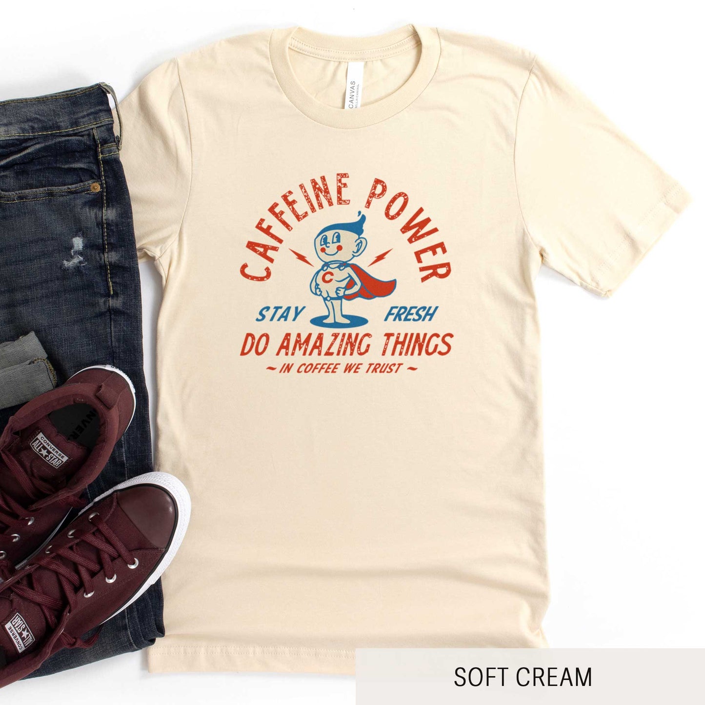 A soft cream Bella Canvas t-shirt featuring a retro coffee mug dressed as a super hero with the words caffeine power, stay fresh, do amazing things, in coffee we trust.
