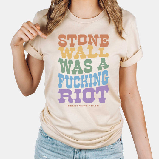A woman wearing a soft cream Bella Canvas t-shirt that says Stonewall was a fucking riot celebrate pride.