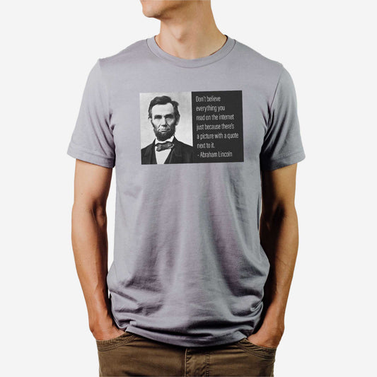 A man wearing a storm Bella Canvas t-shirt featuring a famous photo of Abraham Lincoln with next to it the phrase, don't believe everything you read on the internet just because there's a picture with a quote next to it.