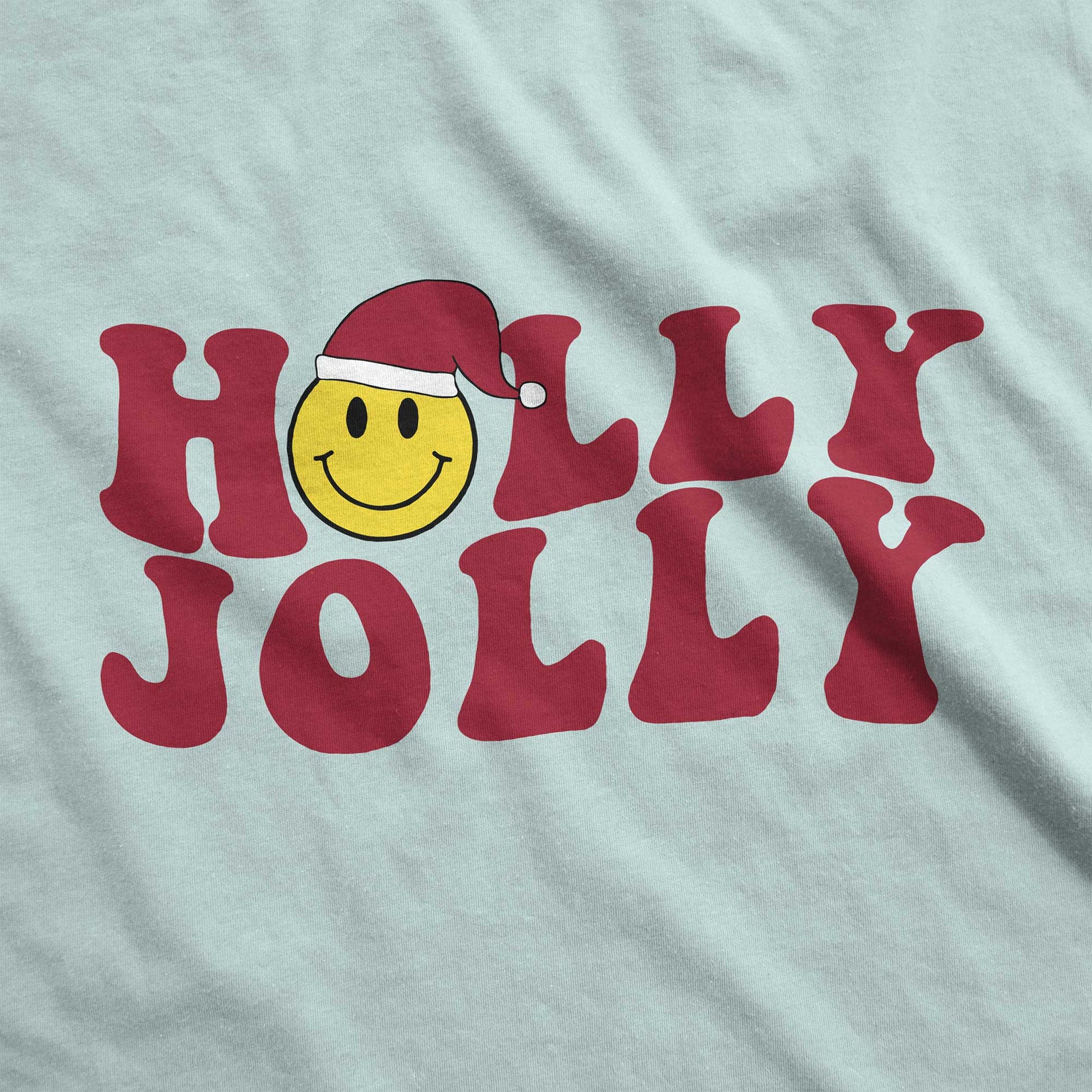 A dusty blue Bella Canvas swatch featuring a yellow smiley face with a santa hat among the words holly jolly.