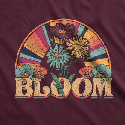 A maroon red Bella Canvas t-shirt featuring a retro styled illustration of flowers and a multi-colored sunray with the words bloom.