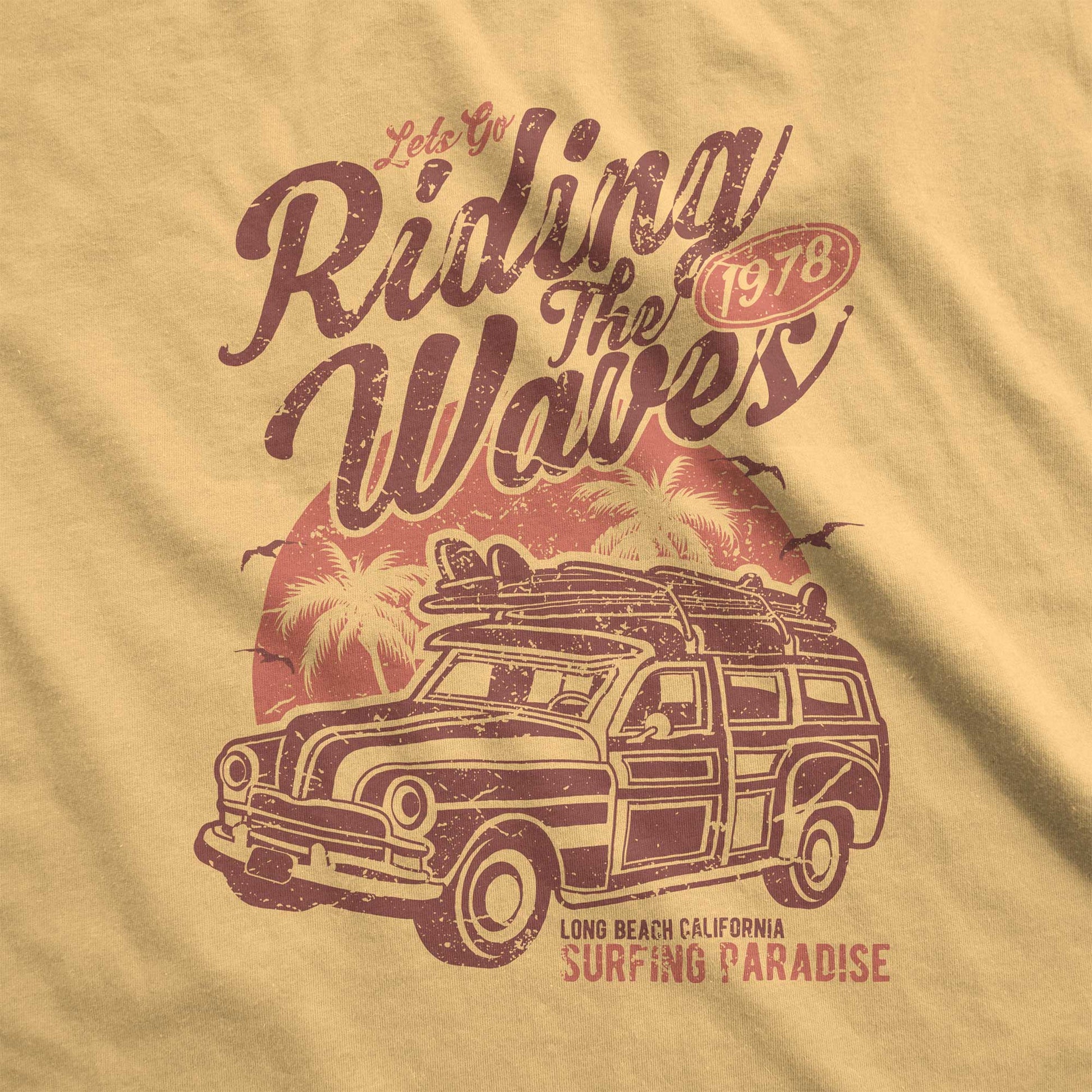 A mustard yellow Comfort Colors swatch featuring a woodie station wagon, a surfboard, palm tress and the words let's go riding the waves