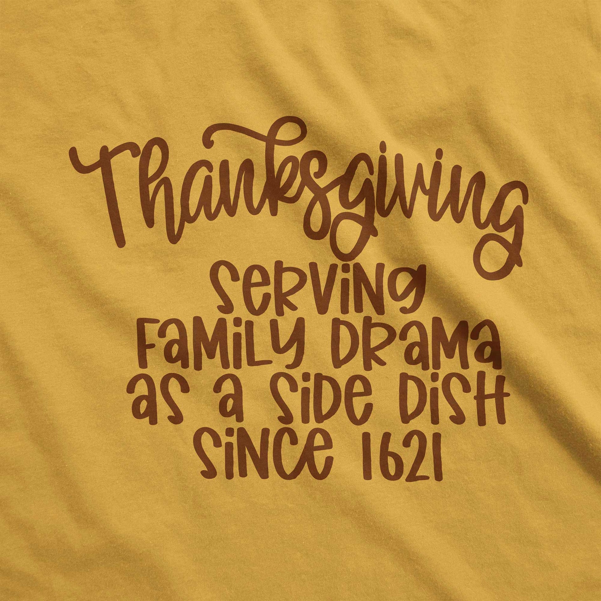 A mustard yellow Bella Canvas swatch featuring the words thanksgiving serving family as a side dish since 1621.