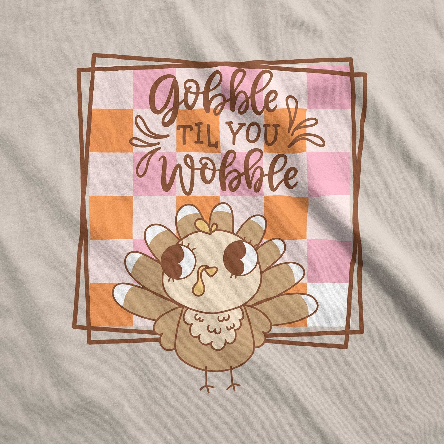 A  sand Gildan swatch featuring a cute cartoon turkey and a fall checkered background with the words gobble til you wobble.