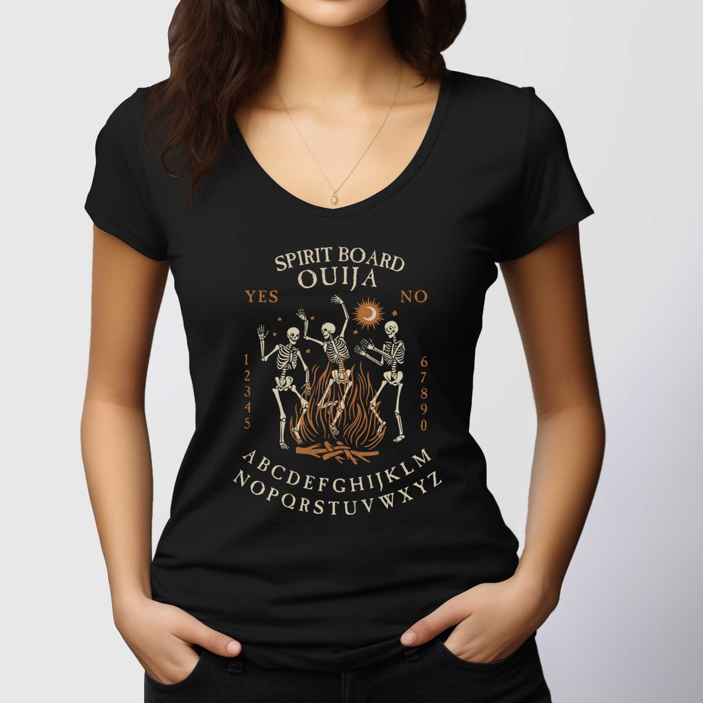A woman wearing a District scoop neck t-shirt with dancing skeletons in front of a fire and an ouija board layout.