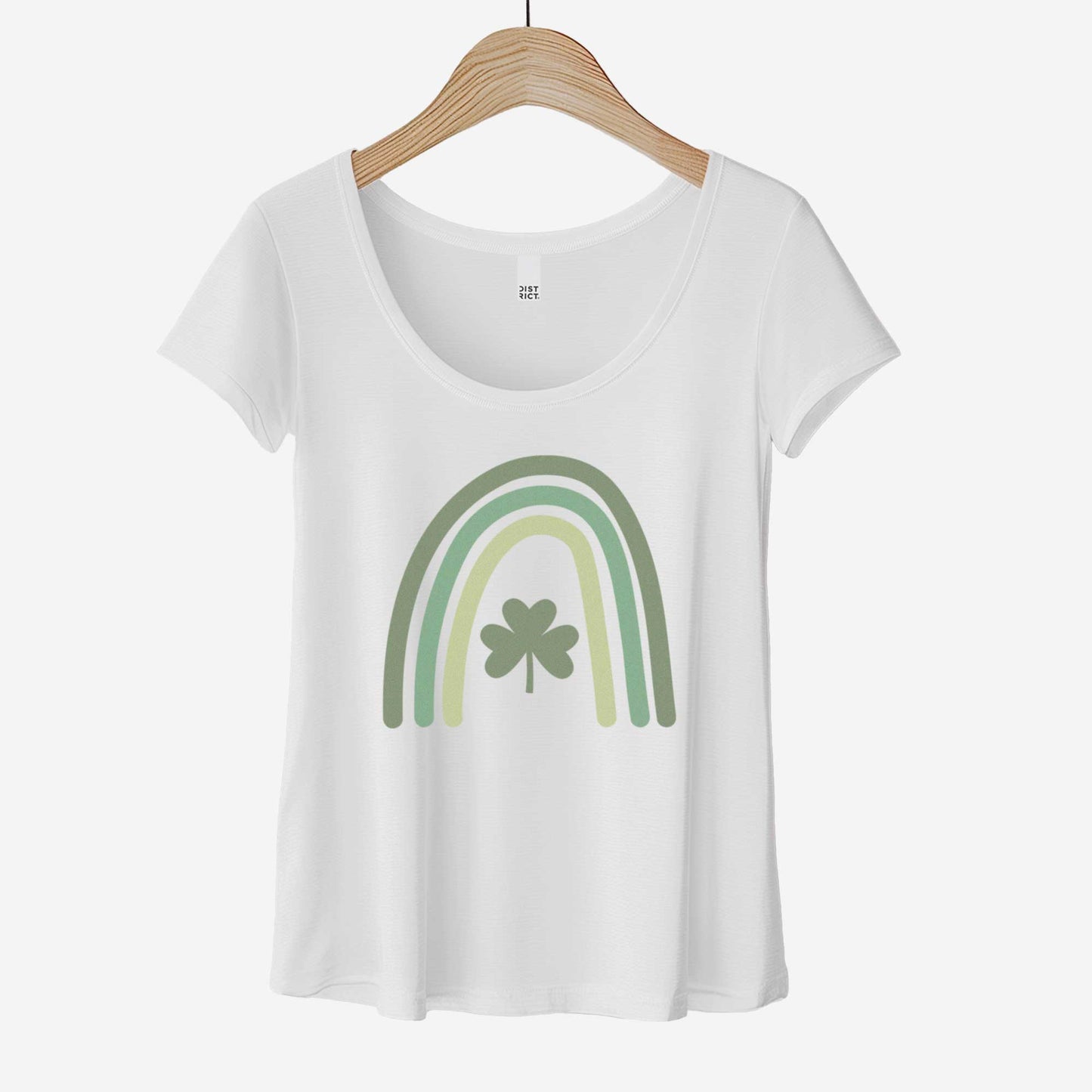 A hanging white District 7501 scoop neck t-shirt featuring a green colored rainbow with a shamrock in the center.