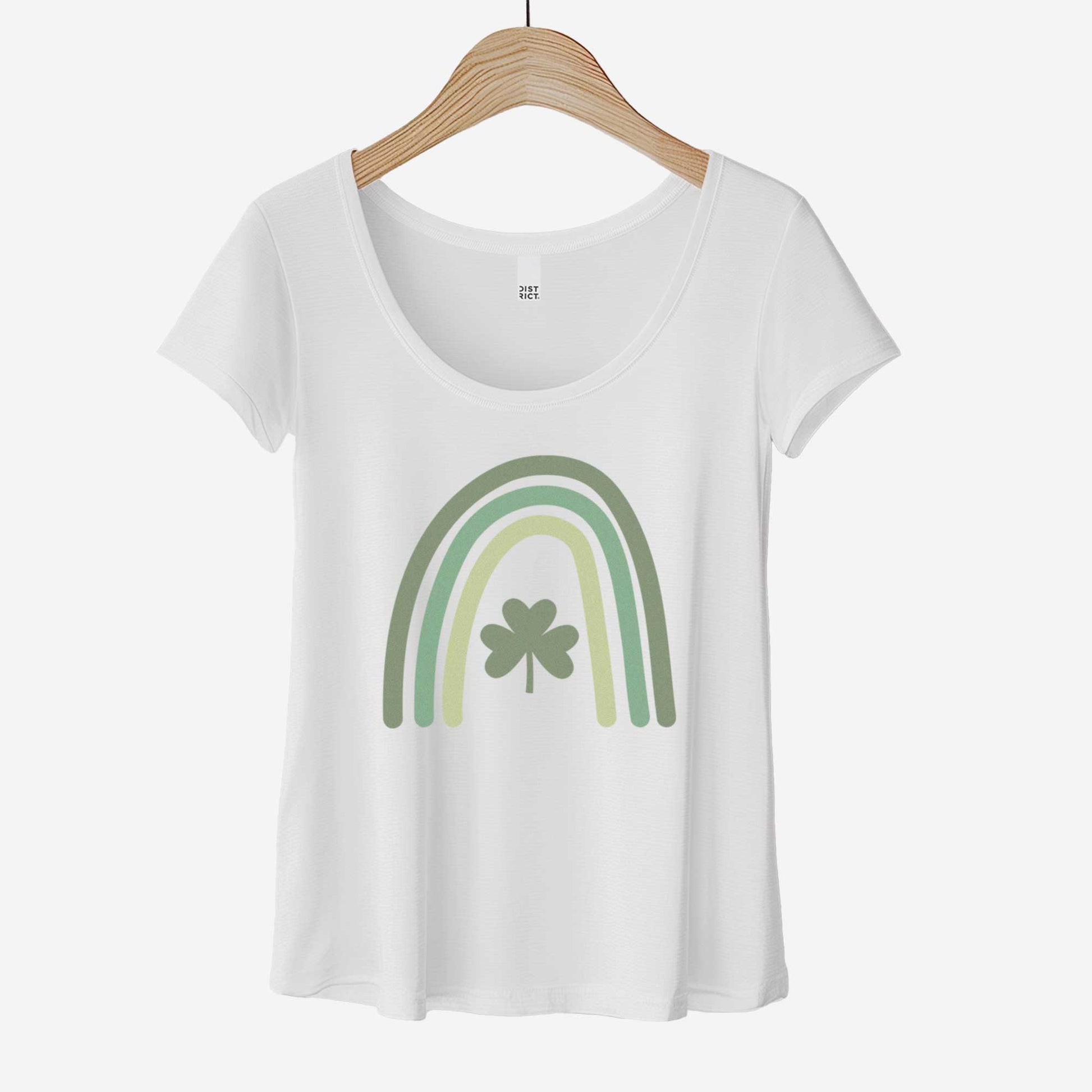 A hanging white District 7501 scoop neck t-shirt featuring a green colored rainbow with a shamrock in the center.