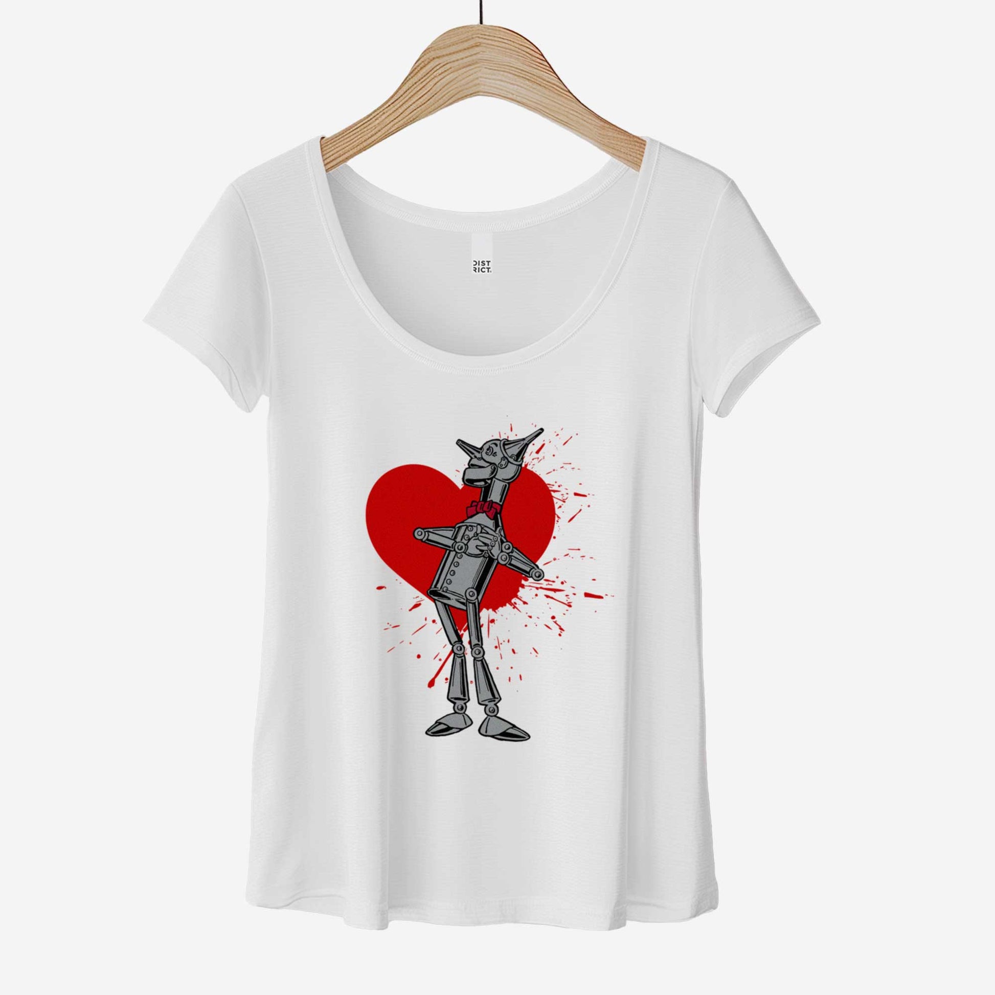 A hanging white District 7501 scoop neck t-shirt featuring a vintage Denslow illustration of the tin man from the Wizard of Oz with a heart symbol spattered behind him.