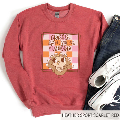 A heather sport scarlet red Gildan sweatshirt featuring a cute cartoon turkey and a fall checkered background with the words gobble til you wobble.