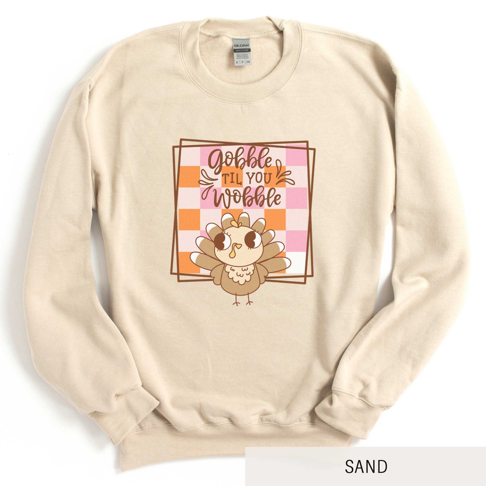 A sand Gildan sweatshirt featuring a cute cartoon turkey and a fall checkered background with the words gobble til you wobble.