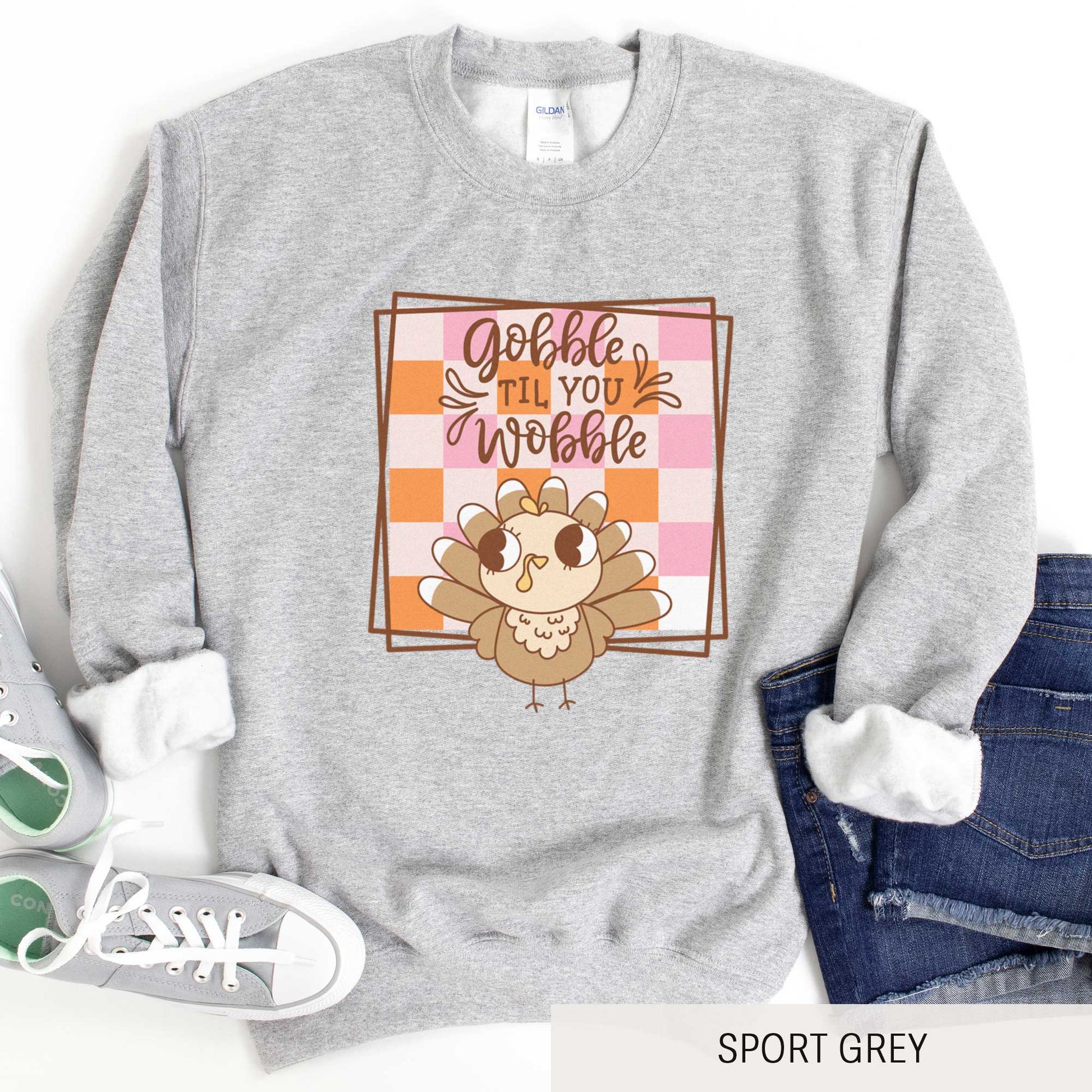 A sport grey Gildan sweatshirt featuring a cute cartoon turkey and a fall checkered background with the words gobble til you wobble.