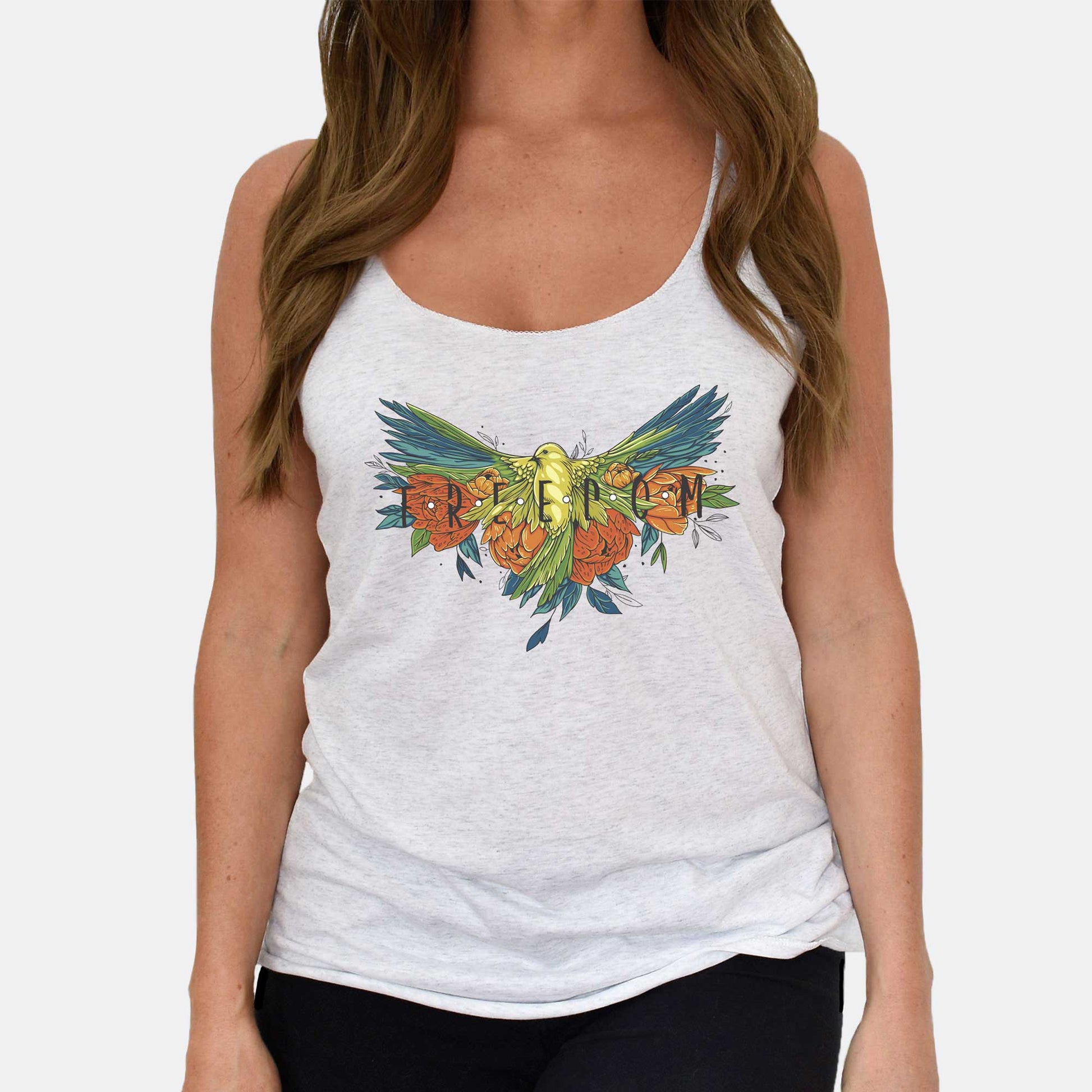 A woman wearing an athletic white Next Level racerback tank top featuring a colorful tattoo style of a bird spreading its wings with the words freedom.