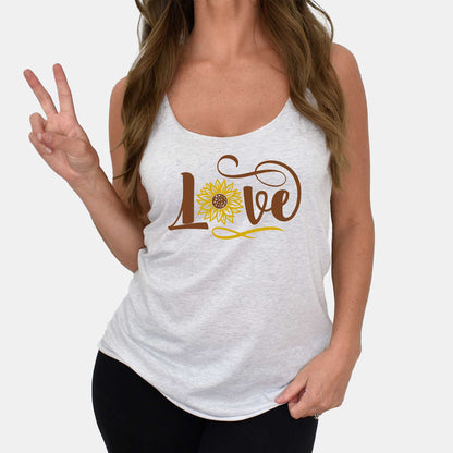 A woman wearing a heather white Next Level racerback tank featuring the words love with a sunflower making the o in the word.