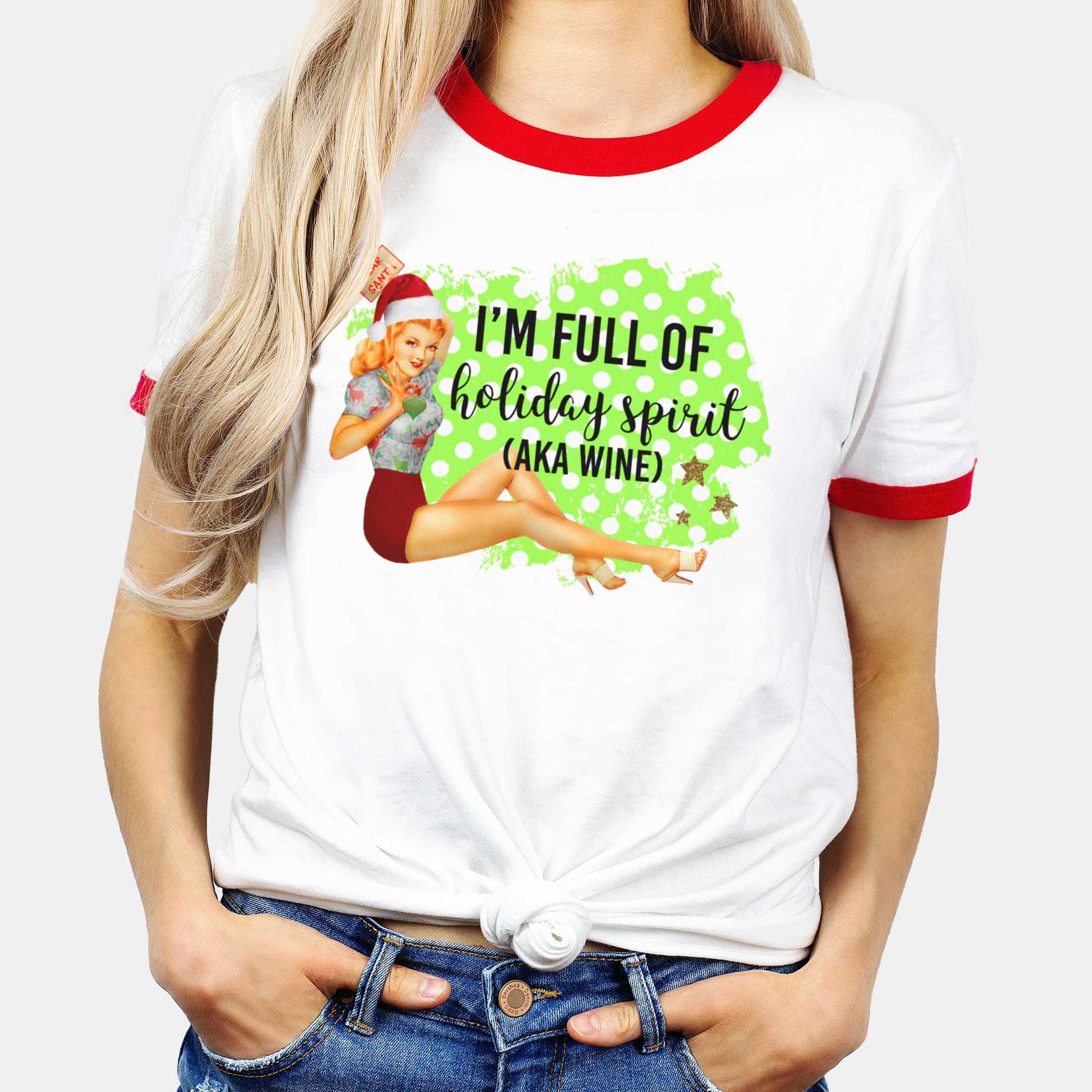 A woman wearing a white with red bands ringer t-shirt featuring a vintage pin-up girl in a holiday outfit and the words i'm full of holiday spirit (aka wine).